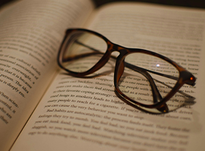 Reading glasses resting flat on an open book with magnified text underneath